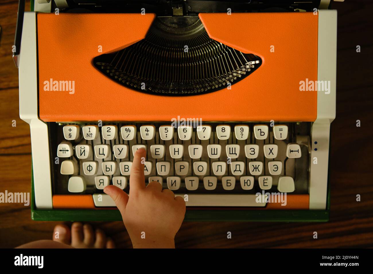 Children's hand presses Russian letter on orange vintage typewriter. Child learns letters.  Stock Photo