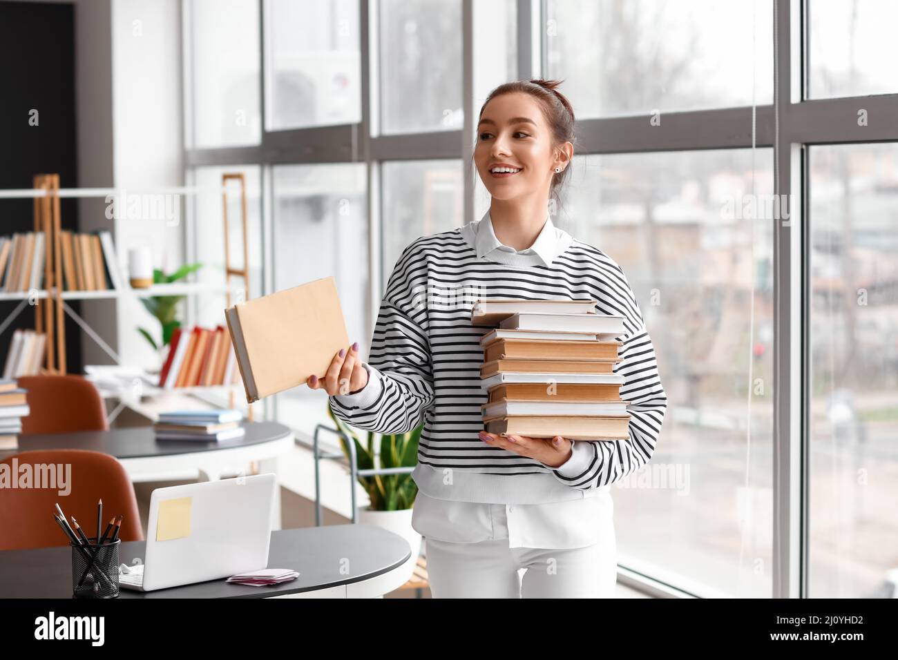 Beautiful female student with stack of books in library Stock Photo - Alamy