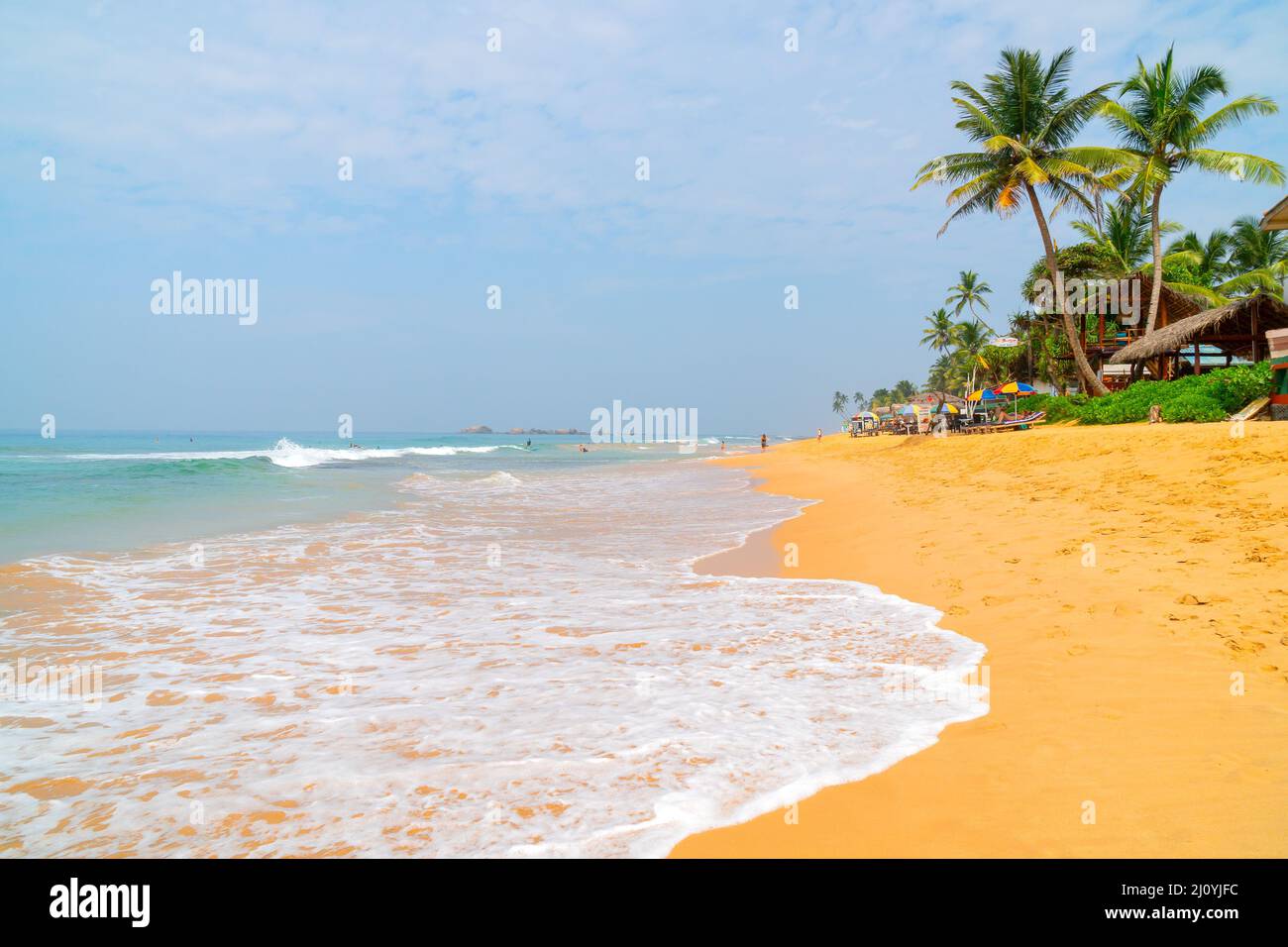 Hikkaduwa, Sri Lanka. March 8, 2018. Beach on the Indian Ocean. Sunny day, yellow sand, palm trees and foam waves. Stock Photo