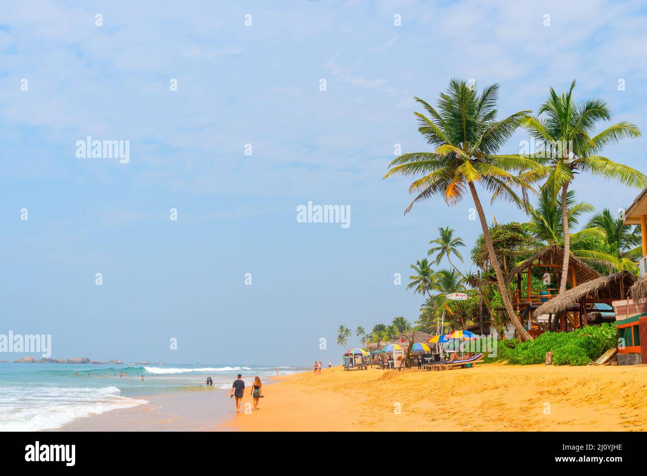 Hikkaduwa, Sri Lanka. March 8, 2018. Beach on the Indian Ocean. Sunny day, yellow sand, palm trees and foam waves. Stock Photo