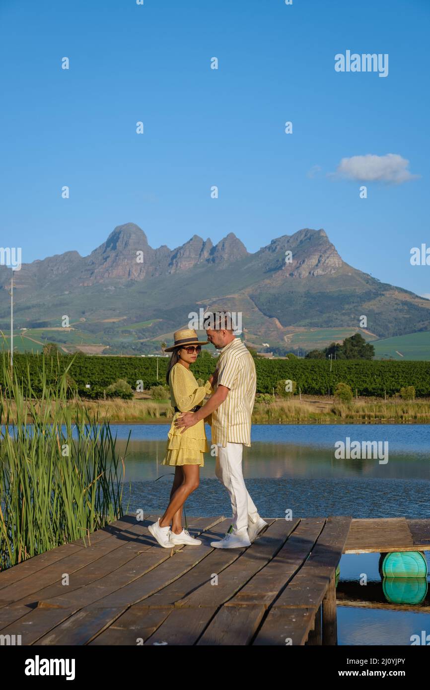 Couple man and woman looking out over lake,Vineyard landscape at sunset with mountains in Stellenbosch, near Cape Town, South Af Stock Photo