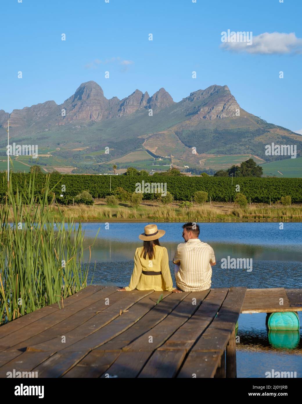Couple man and woman looking out over lake,Vineyard landscape at sunset with mountains in Stellenbosch, near Cape Town, South Af Stock Photo