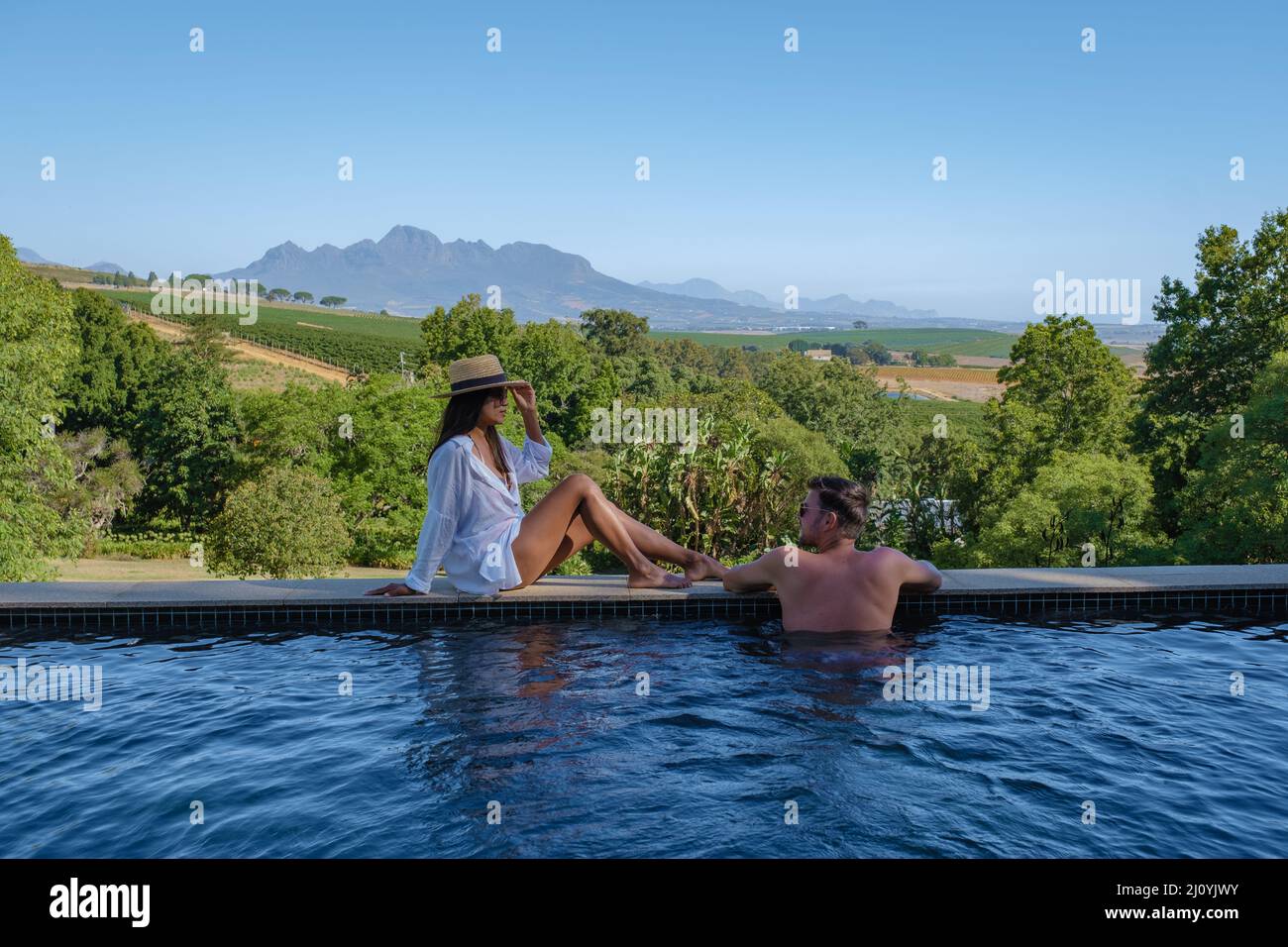 Couple man and woman in swimming pool looking out over the Vineyards and mountains of Stellenbosch South Africa Stock Photo