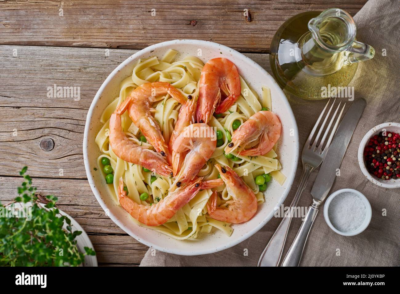 Shrimp, pasta tagliatelle, green peas, dill. White plate on old rustic wooden table Stock Photo