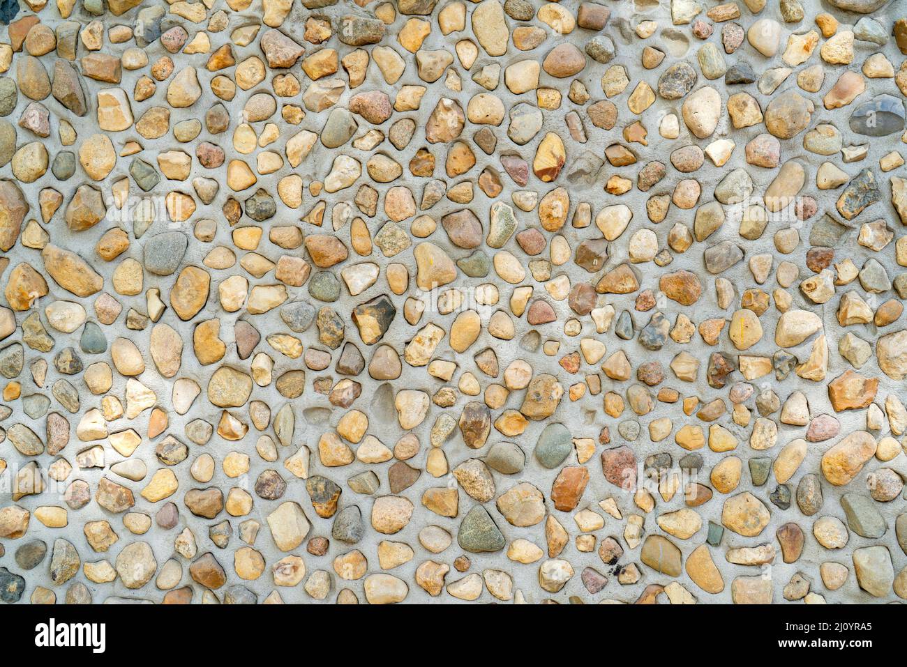 Stones in concrete. Gray texture of uneven plaster on the wall of the house. Stock Photo
