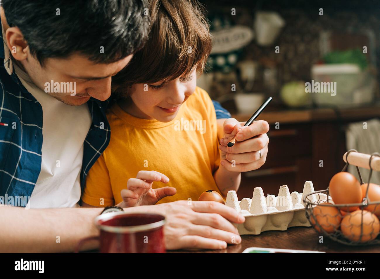 Easter day. Male Father and son painting eggs on wooden background. Family sitting in a kitchen. Preparing for Easter, creative homemade decoration Stock Photo