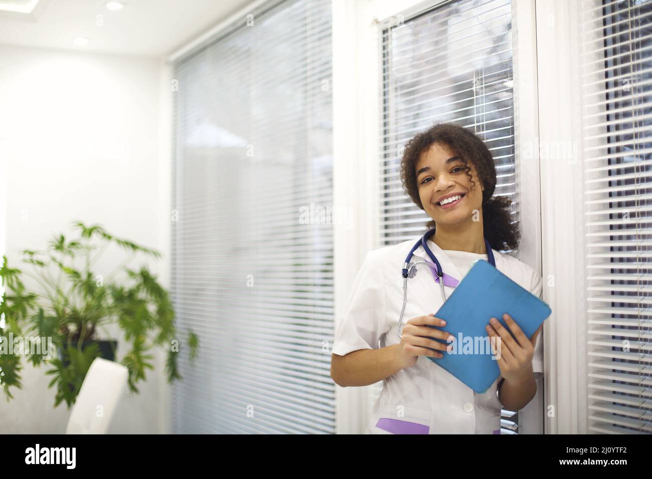 Happy african american female doctor with stethoscope around neck holding digital tablet and smiling Stock Photo
