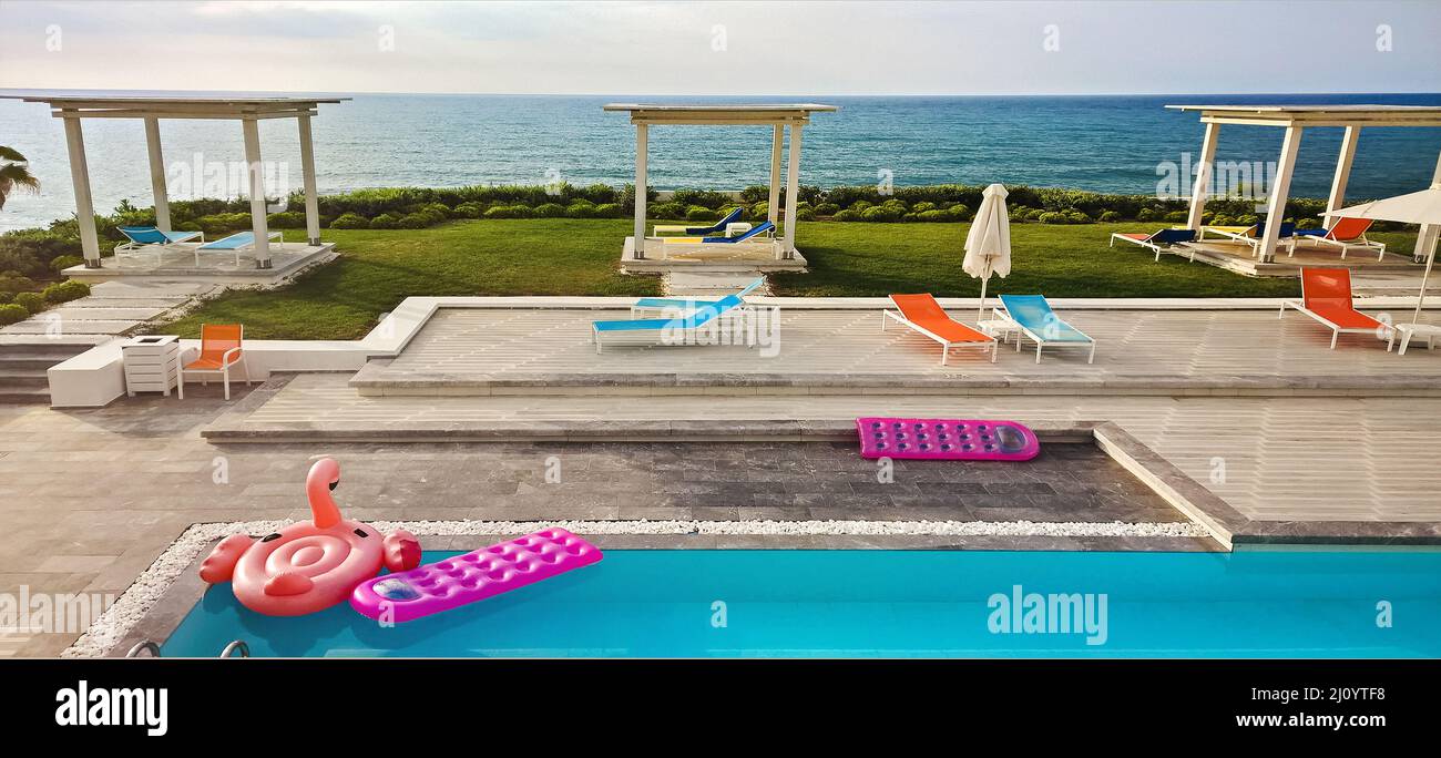 Inflatable float rubber objects in the form of a pink mattress and flamingo in the blue water of the pool in sunset Stock Photo