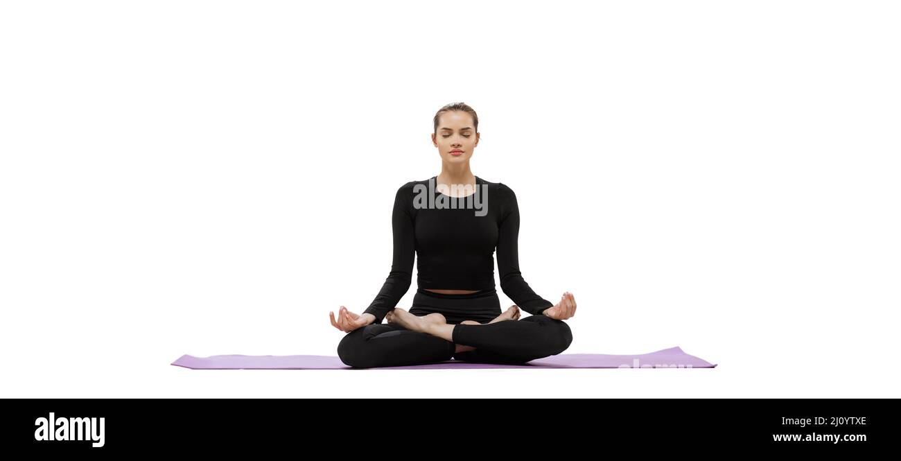 Portrait of young sportive woman sitting in lotus yoga pose on mat and ...
