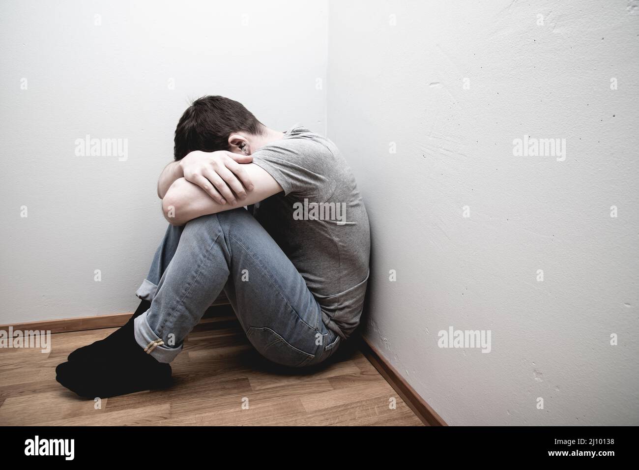 Depressed male sitting in the corner of a room hugging his knees and ...