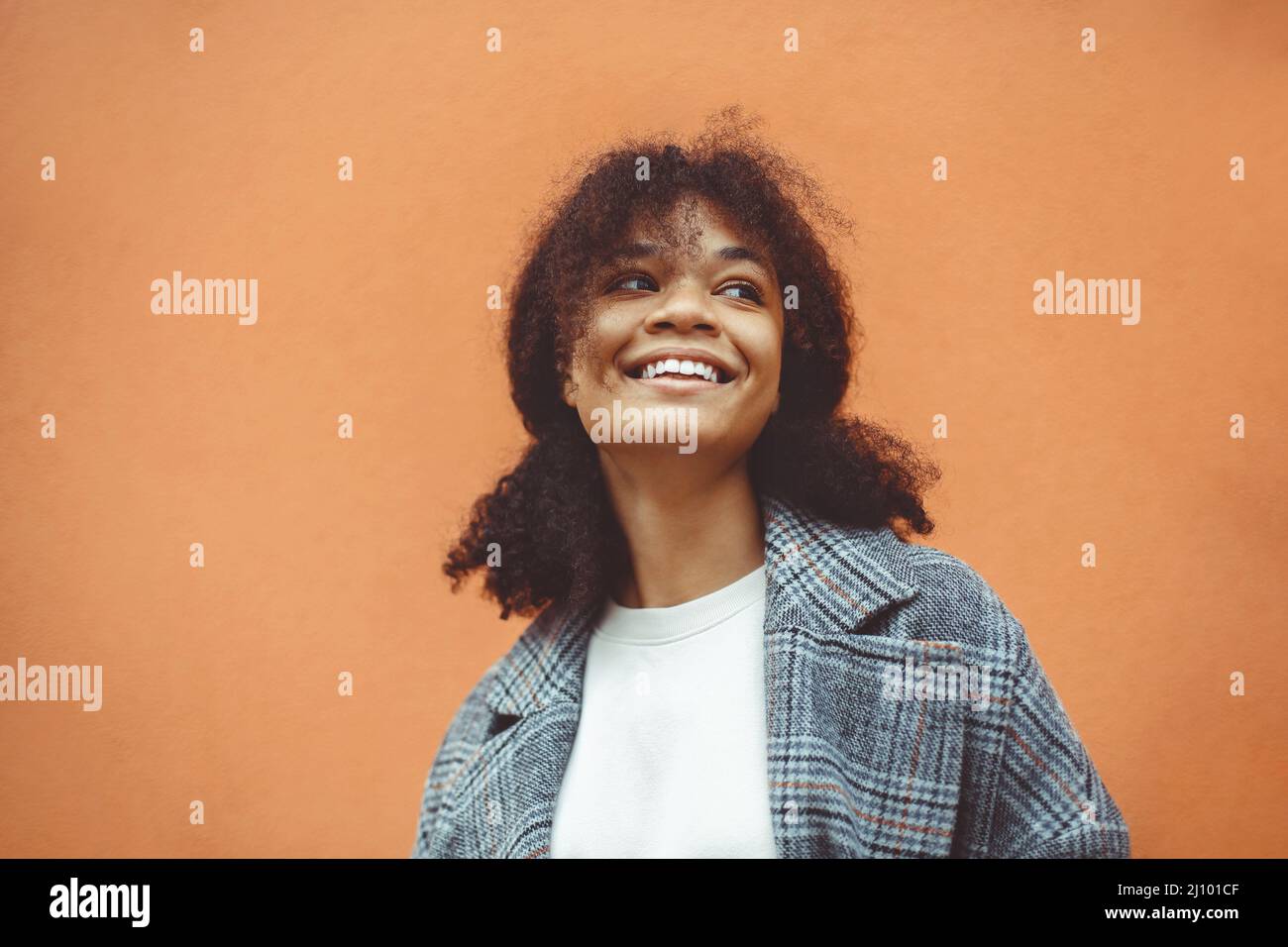 Happy African ethnicity girl with dark curly hairstyle in stylish coat looking aside and smiling Stock Photo