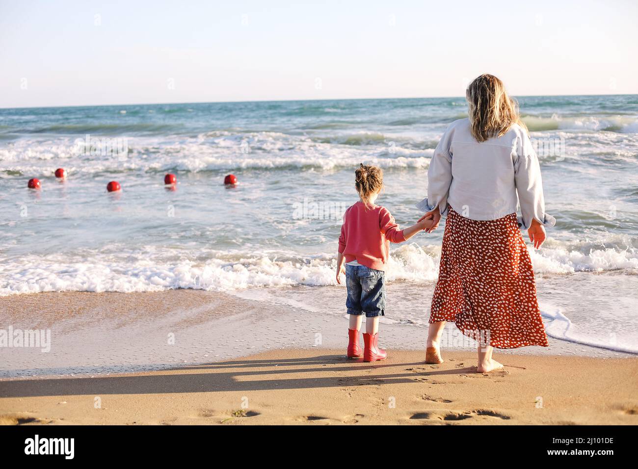 Young happy mother with smiling daughter running towards her on sunny beach Stock Photo