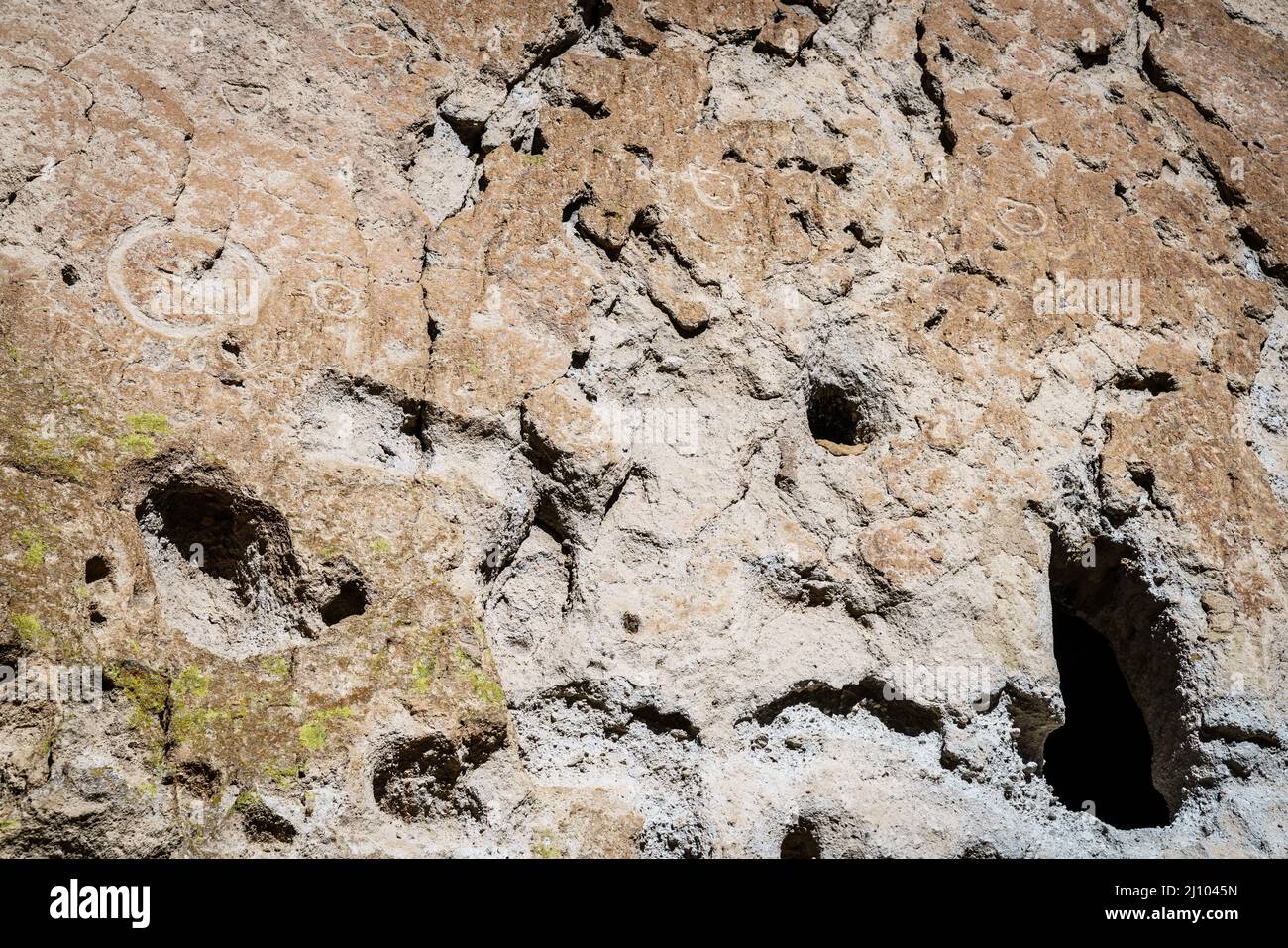 An ancient dwelling in the cliff face surrounded by petroglyphs in Bandelier National Monument, New Mexico Stock Photo
