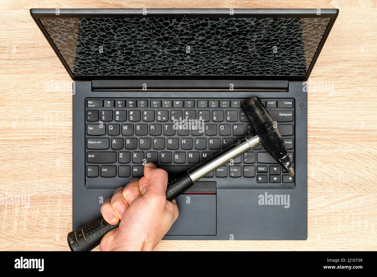 Hand with a hammer and laptop with a broken screen. Concept of rough