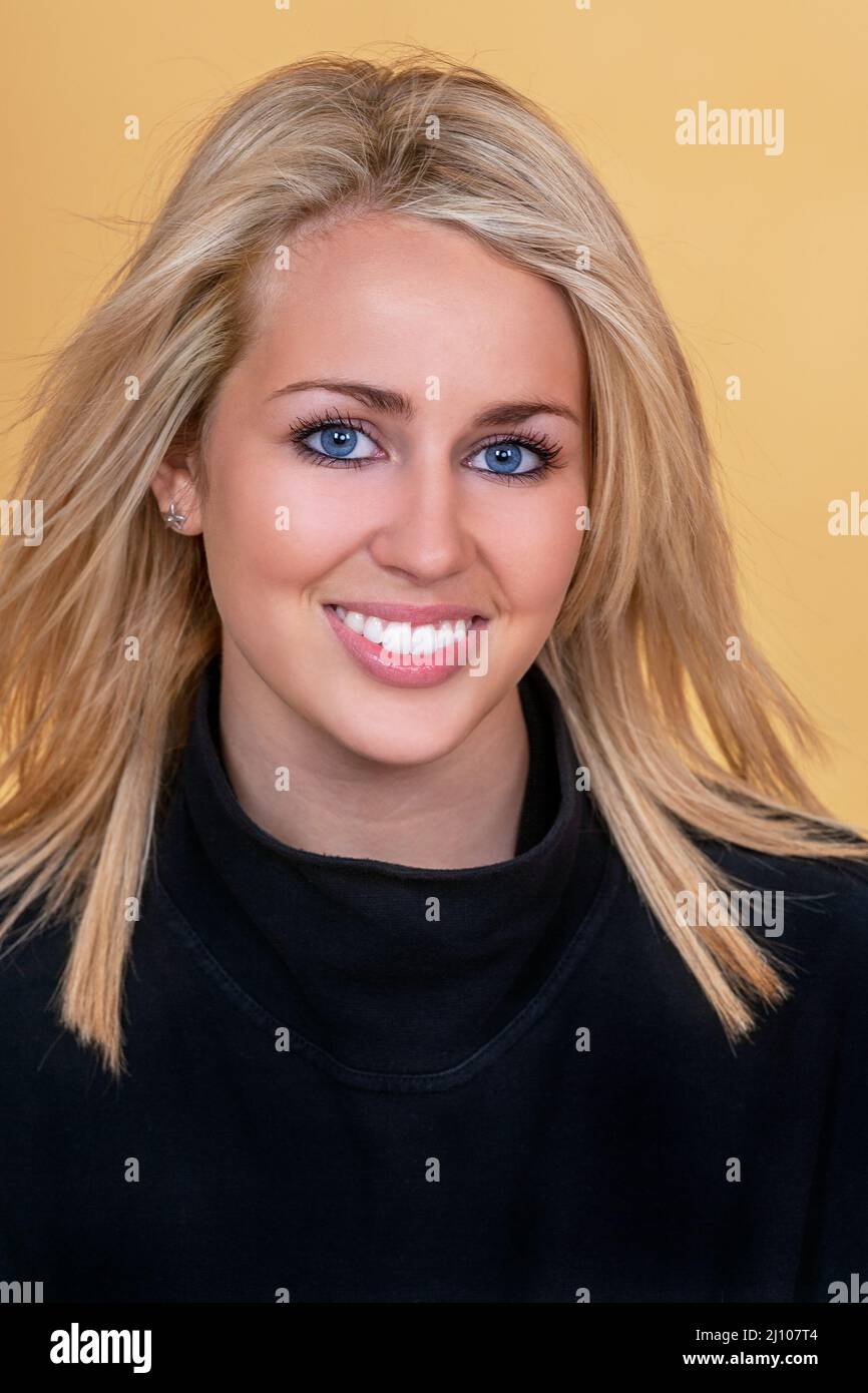 Studio shot with a yellow background of a beautiful blonde haired blue eyed female model girl young woman with perfect teeth Stock Photo