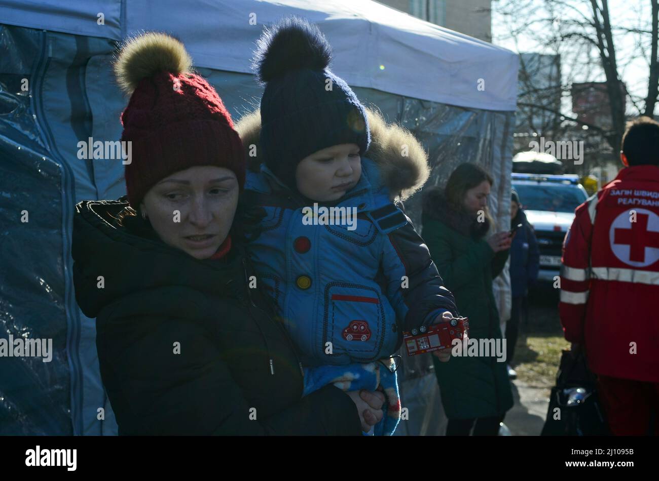 Non Exclusive: KYIV, UKRAINE - MARCH 20, 2022 - A woman holds a baby boy clutching a toy fire engine outside a residential building damaged as a resul Stock Photo