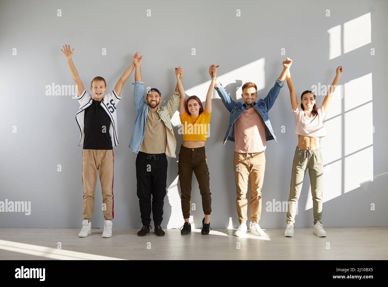 Group of happy young people in casual wear standing in row, holding ...