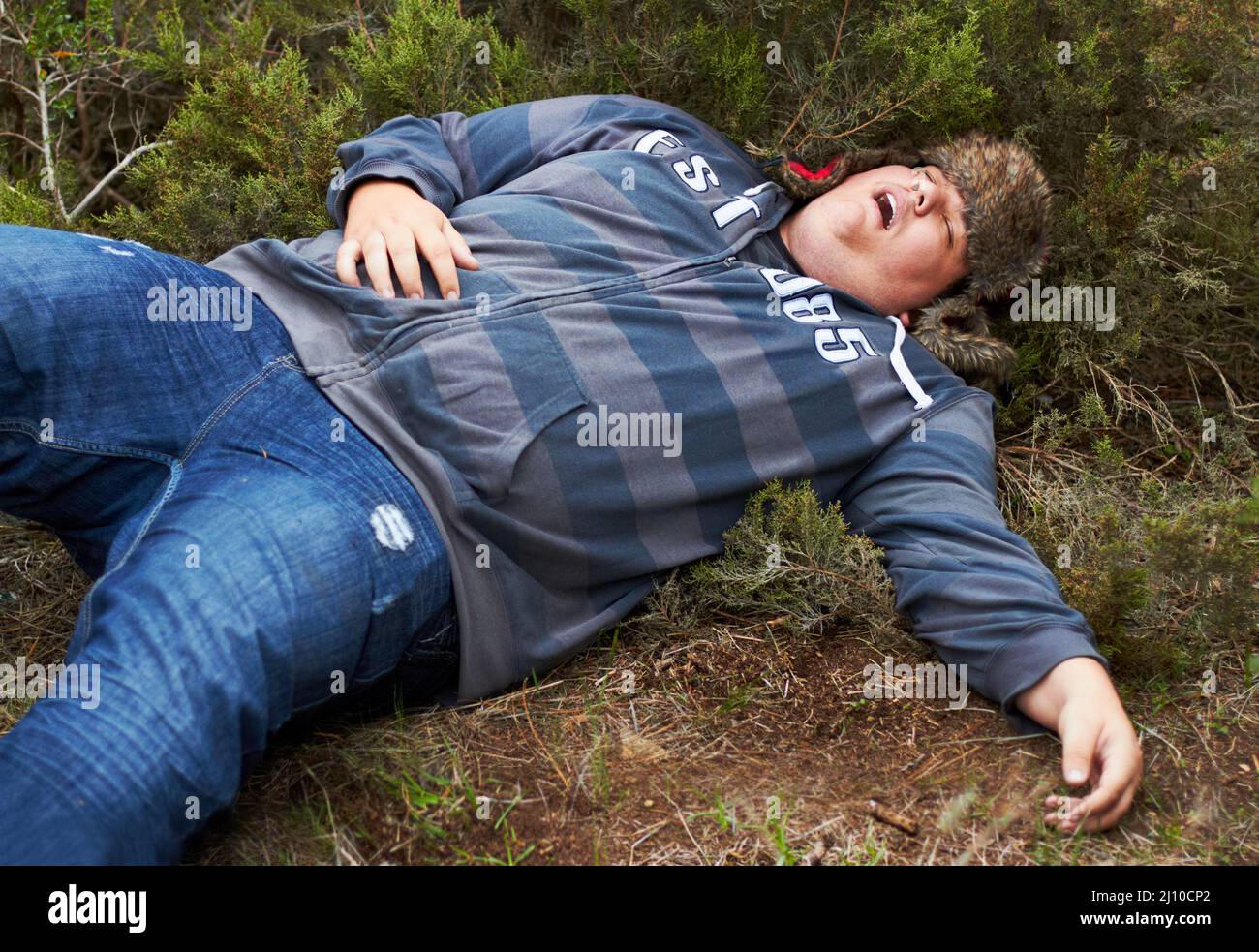 Suffering the consequences of a wild night.... An obese young man lying passed-out outside in the bushes. Stock Photo