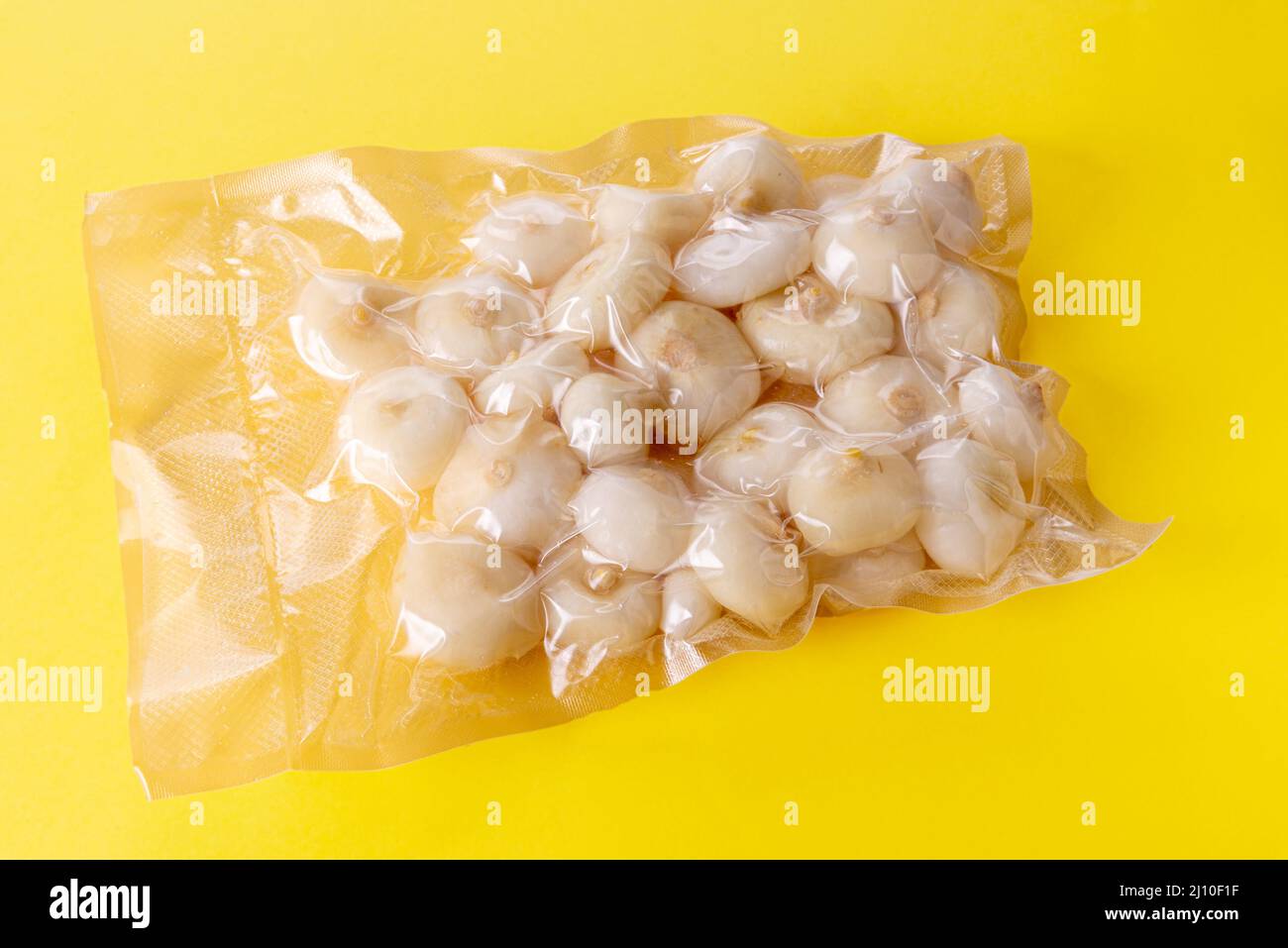 Small flat onions (in Italy called borettane onions) in vacuum packed sealed for sous vide cooking isolated on yellow background Stock Photo