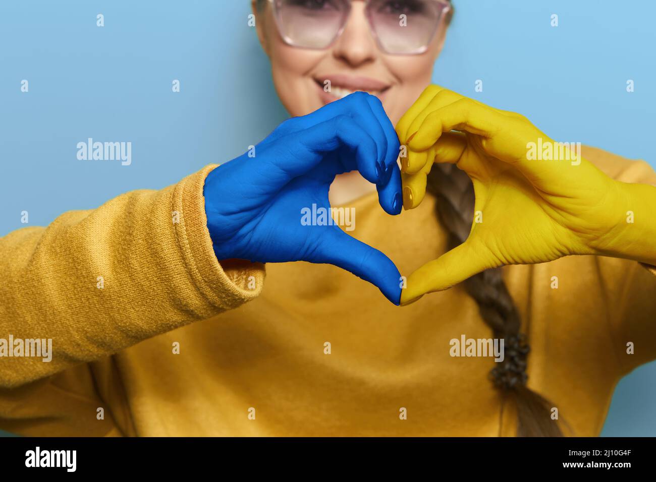Portrait of girl showing heart shape Ukrainian yellow and blue flag on hands forming a heart. Ukraine support Stock Photo