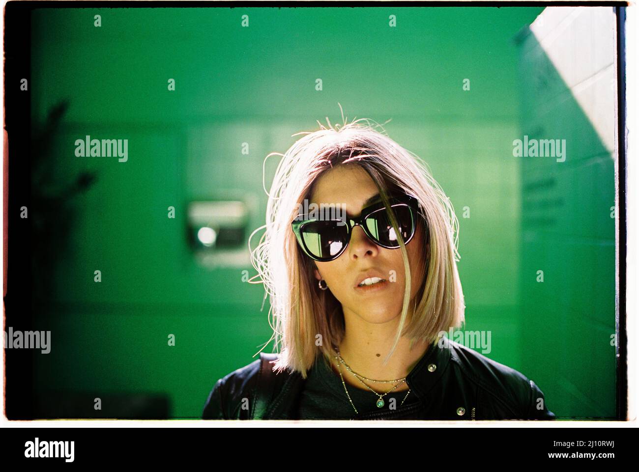 Blond woman on a green room with sunglasses and backlight Stock Photo
