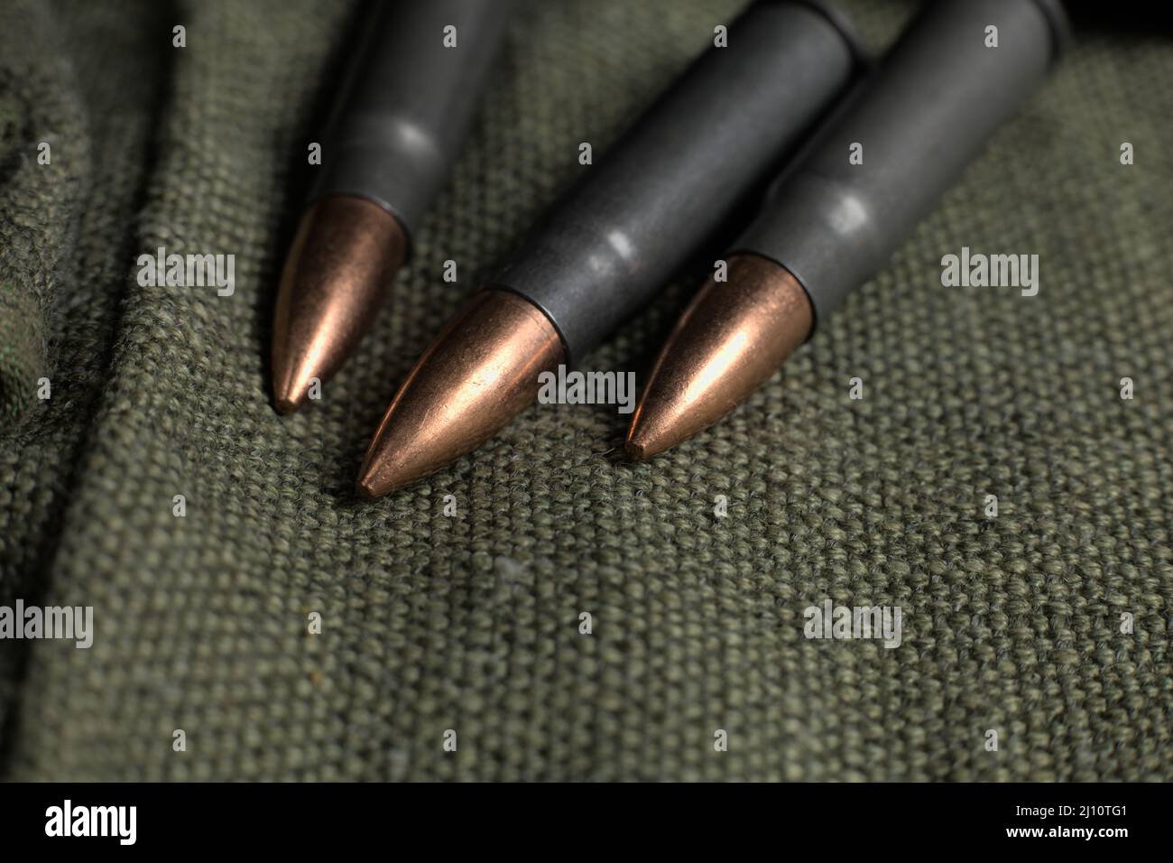 Three Ak-47 (7,62x39mm) cartridges lying on a piece of military canvas, close-up photography Stock Photo