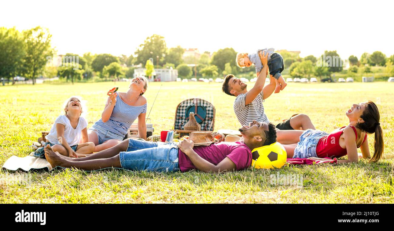 Young multiracial families having fun playing with kids at pic nic garden party - Multiethnic joy and love concept with mixed race people together wit Stock Photo
