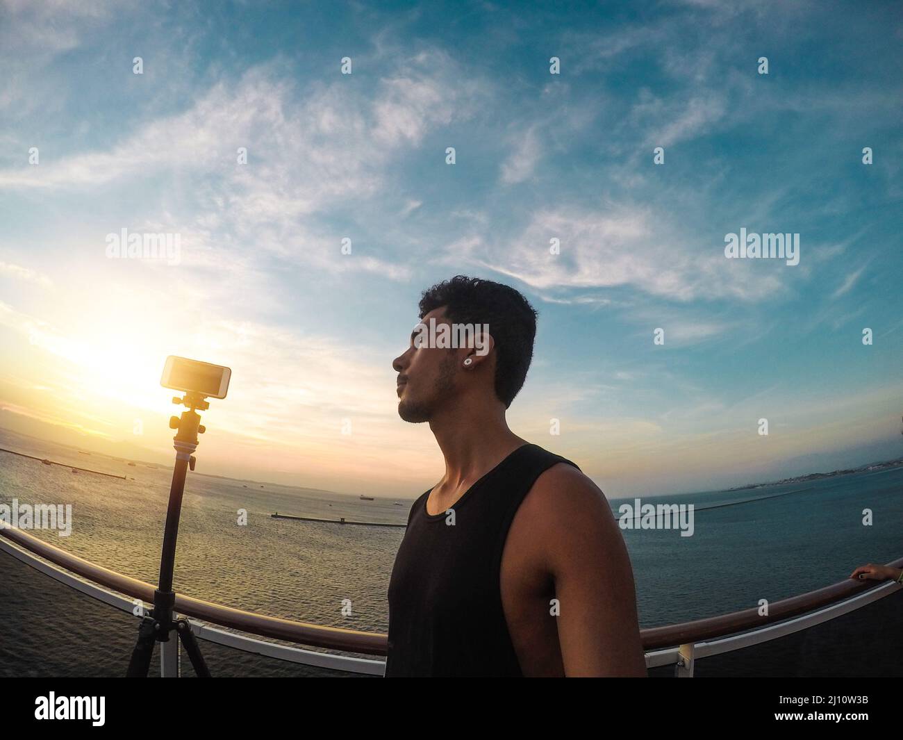 Portrait of a young black male tourist on the deck of a cruise ship in front of a sunset sky. African tourist on the beach trip. Stock Photo