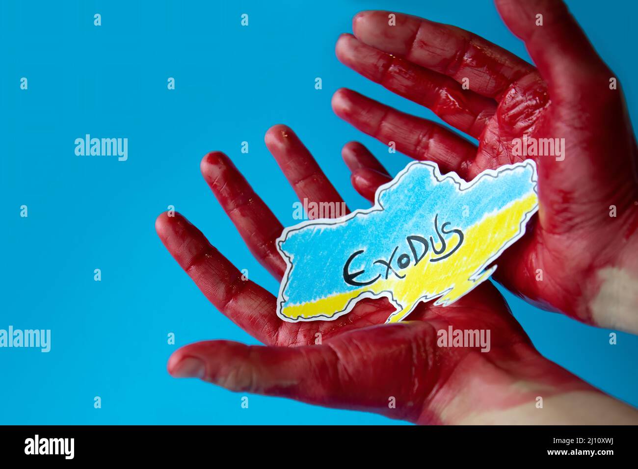 bloody hands on a blue background holding a paper cutout of the map of ukraine painted in the colors of its flag. mass exodus of civilian citizens. Stock Photo