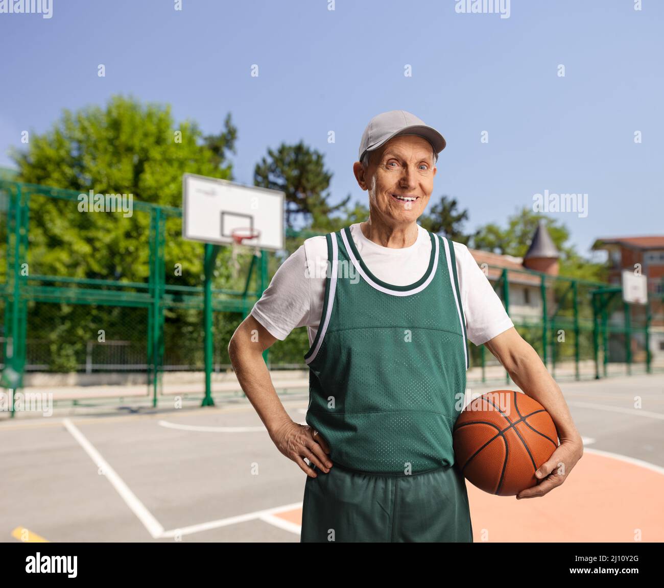 Smiling elderly man holding a basketball on an outdoor basketball court Stock Photo