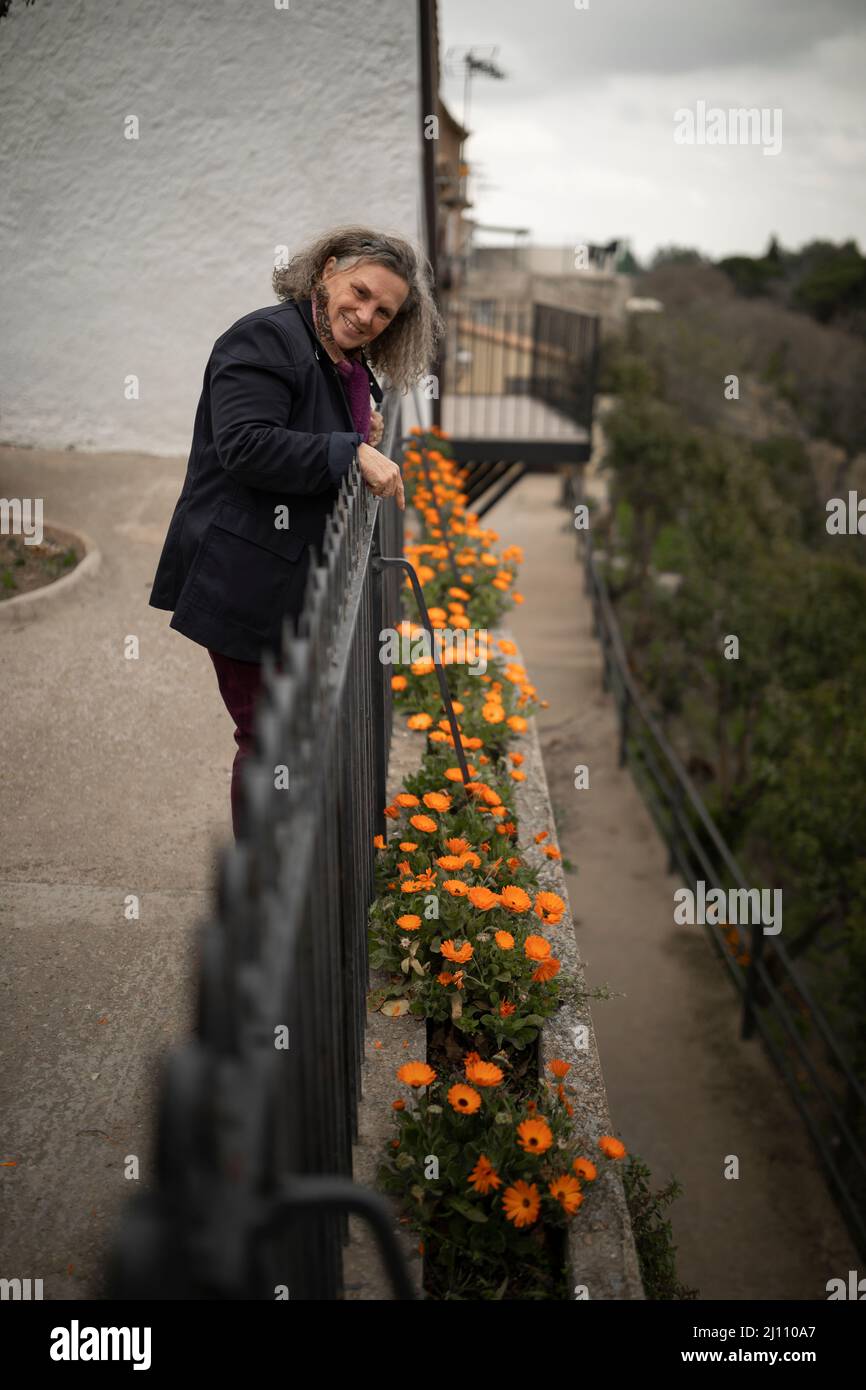 A 60-year-old woman with gray hair looks at orange flowers in a small village, Malejan, in the province of Zaragoza, Aragon, Spain Stock Photo