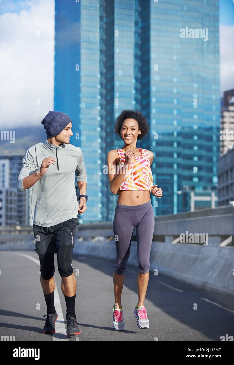 He almost keeps pace with me. Shot of two friends jogging together through the city streets. Stock Photo