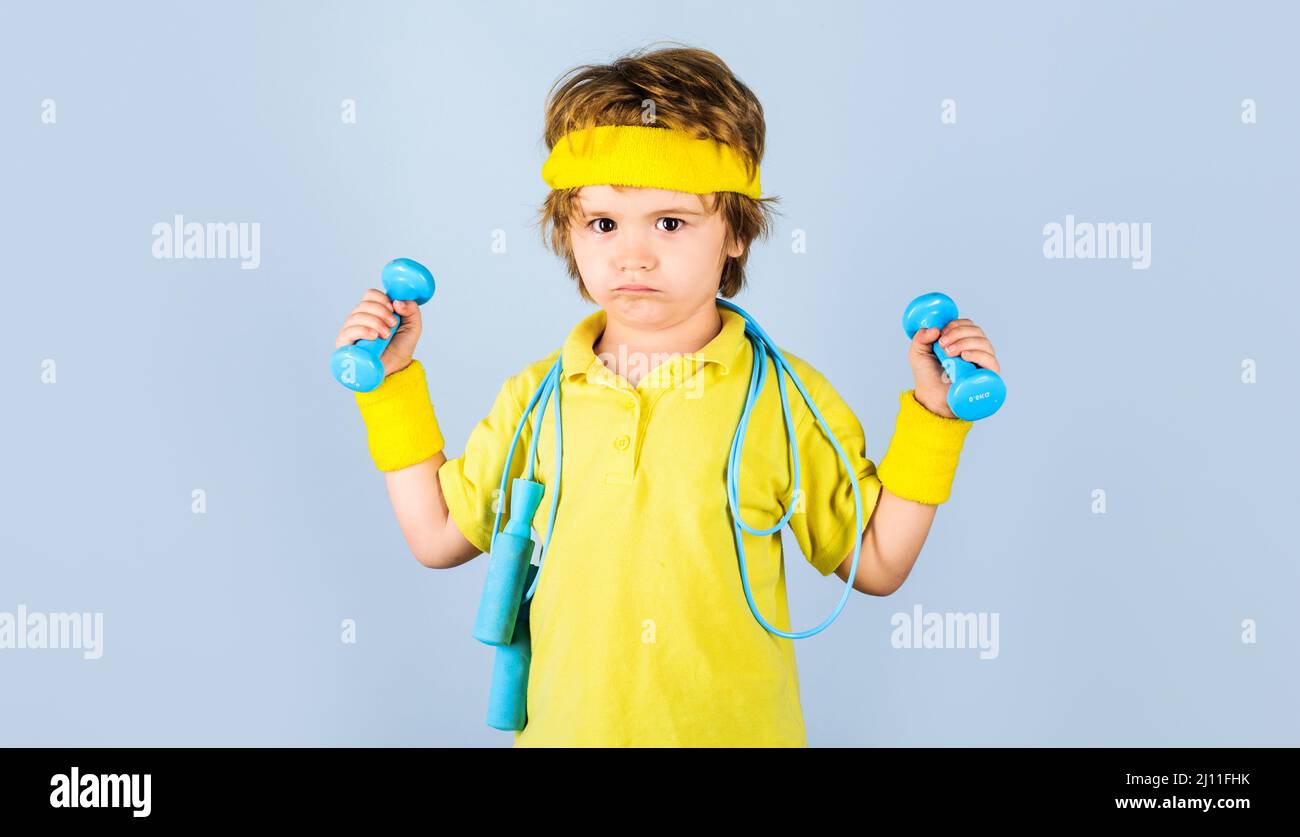 Child in sportswear with skipping rope and dumbbells. Sporty kid boy with jump rope and dumbbell. Stock Photo