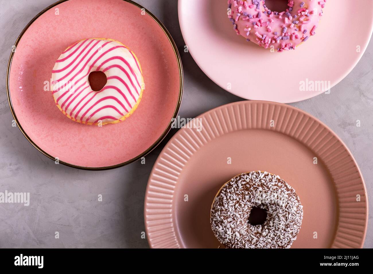 Three glazed donuts lie on tall pink plates Stock Photo