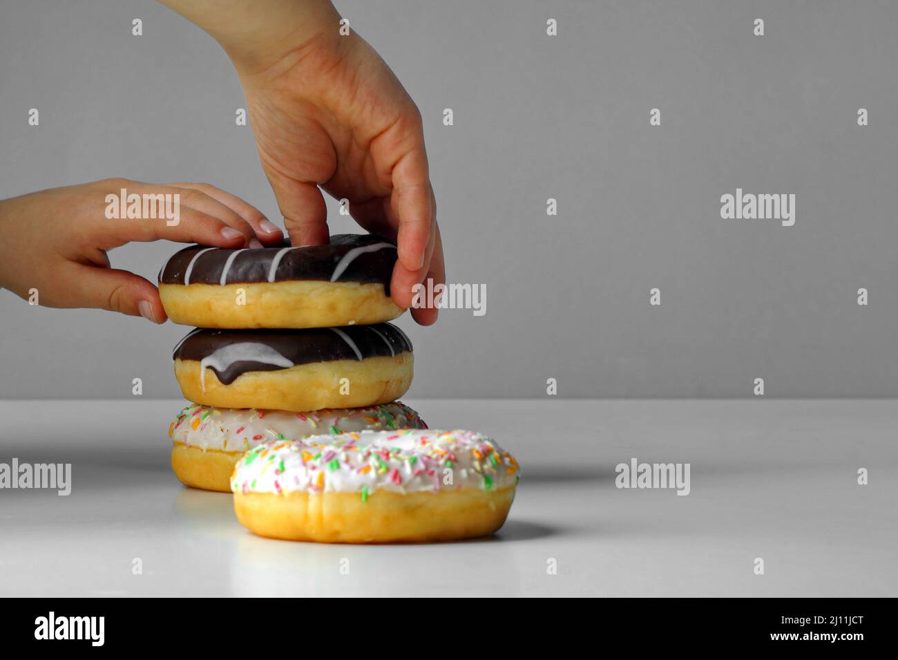 Child lays fresh tasty donuts with multicolored sprinkles and chocolate, builds a tower from them Stock Photo