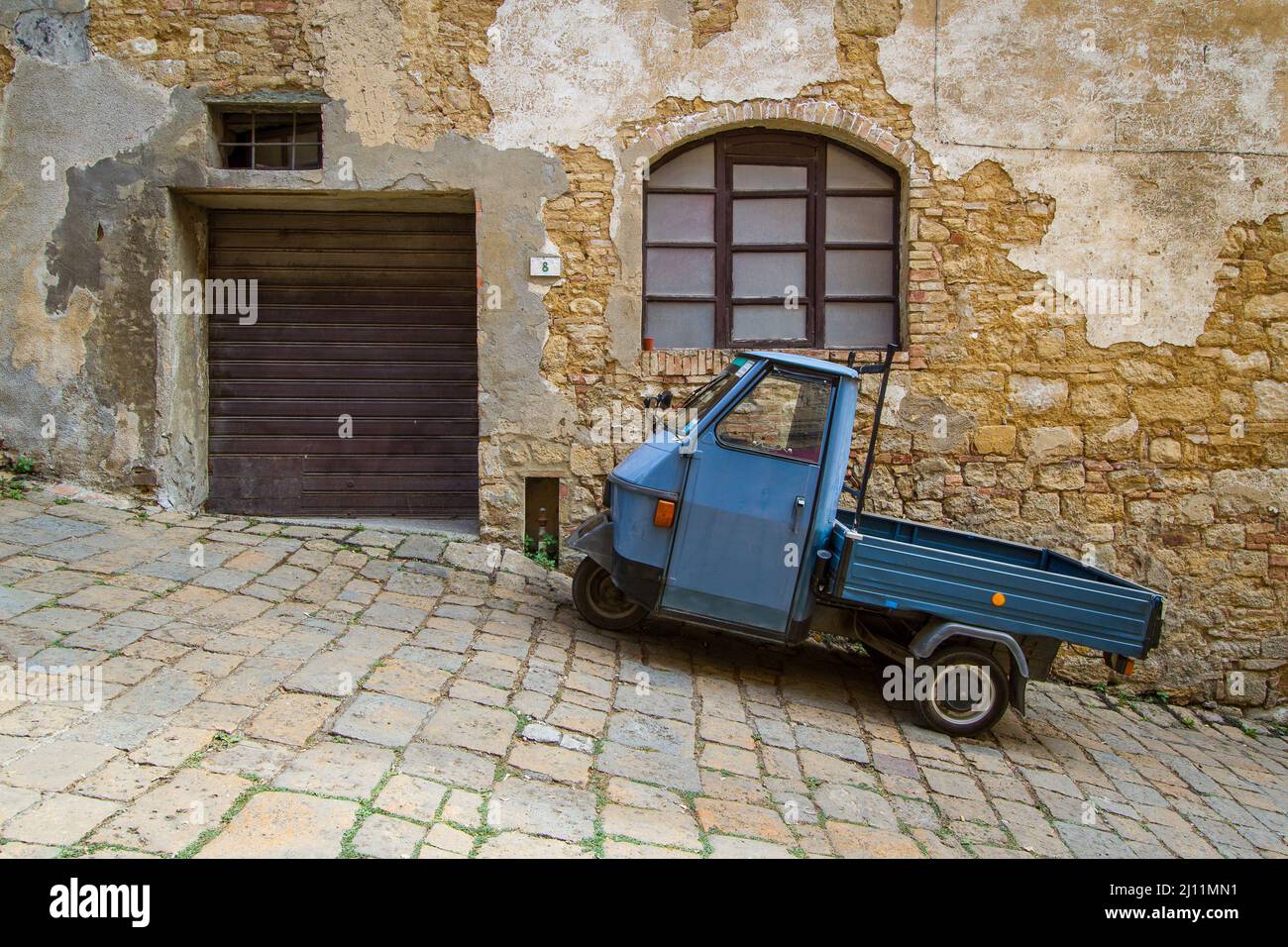 Stereotype scene on the streets of Volterra with a parked Piaggio Ape in front of an old rural building Stock Photo