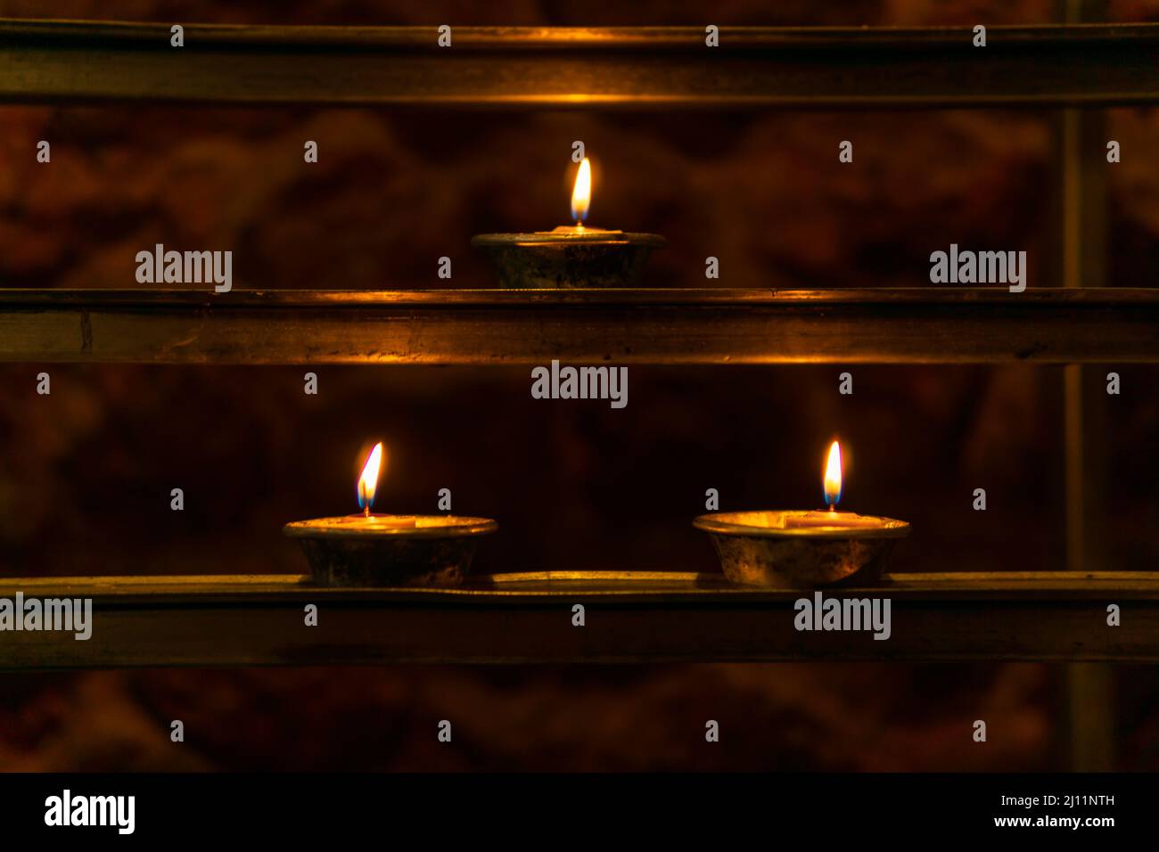 Three lit votive candles on a votive candle rack in a Catholic church