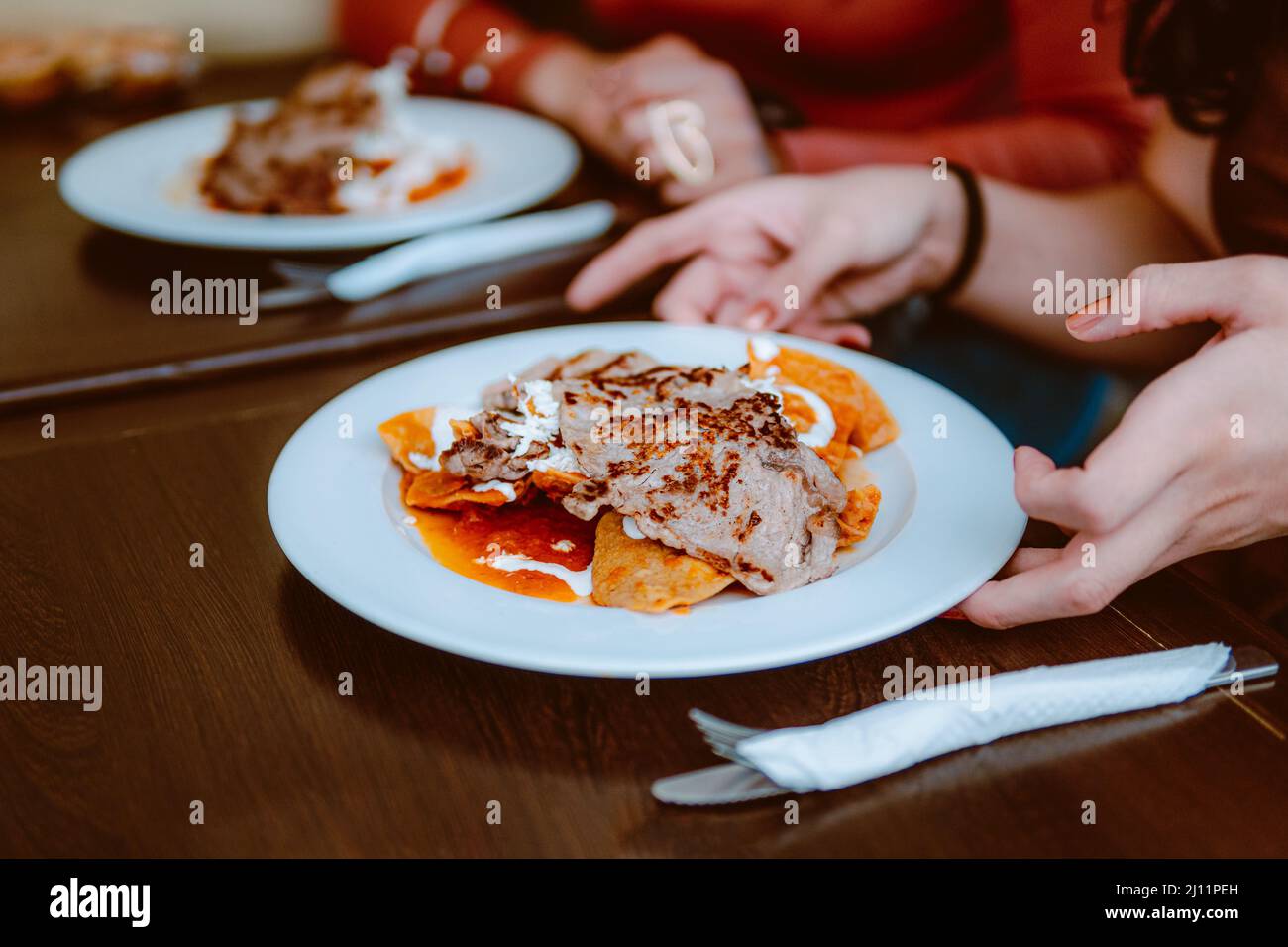 In a restaurant they serve a plate of chilaquiles with cream, cheese and red sauce, a delicious Mexican dish. Stock Photo