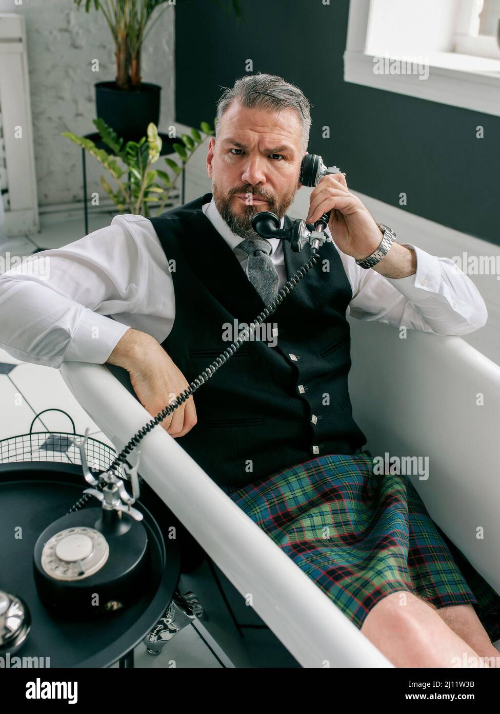 handsome mature courageous stylish man scotsman in kilt and suit talking on the phone from home. Style, fashion, lifestyle, lockdown, culture, ethnic Stock Photo
