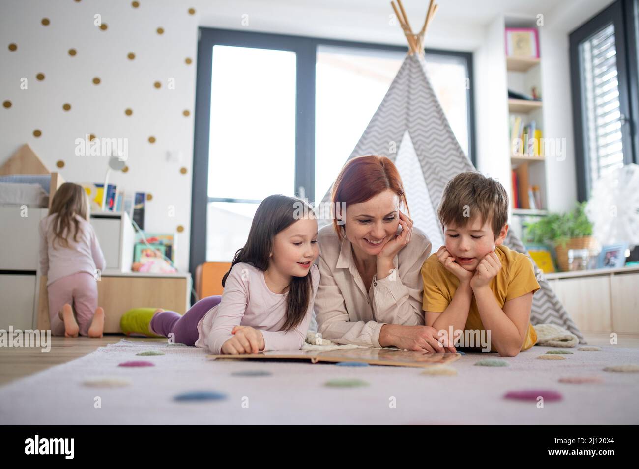 Cheerful mother of three little children reading them book at home. Stock Photo