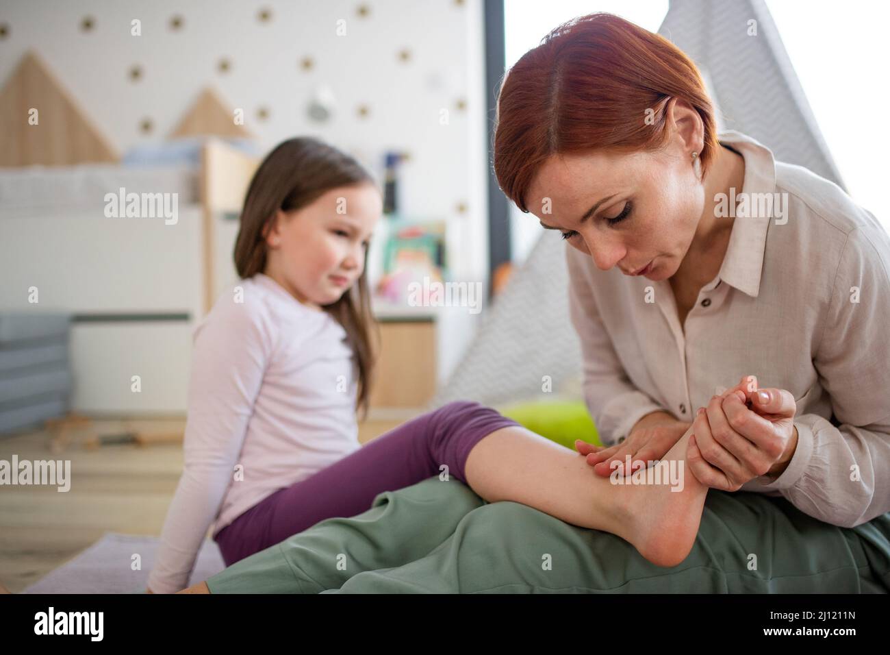 Mother blowing her little daughter's hurt ankle. Stock Photo