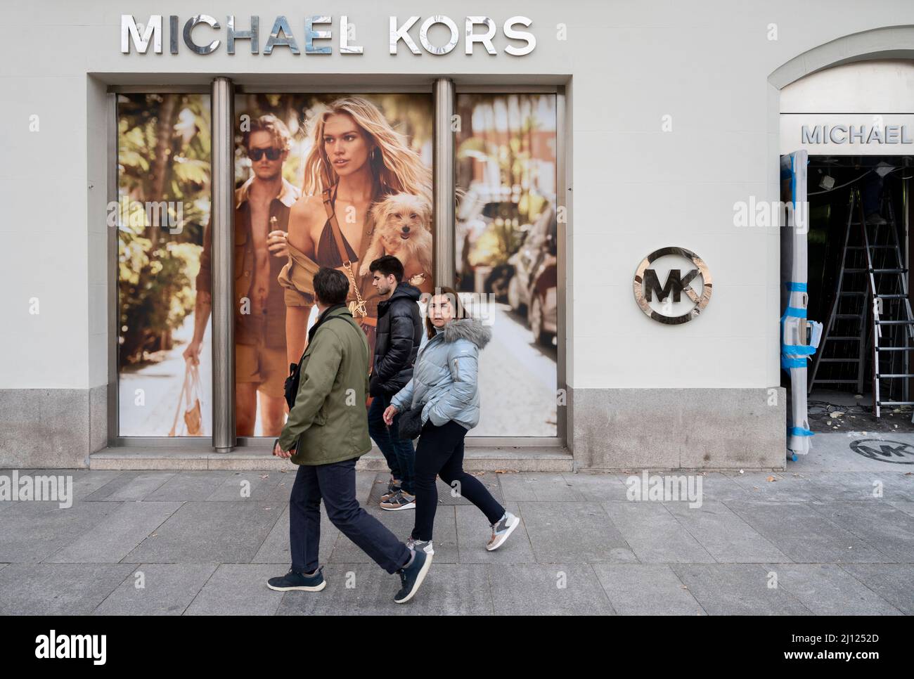 Pedestrians walk past the American clothing fashion store brand Michael Kors  (MK) logo in Spain Stock Photo - Alamy