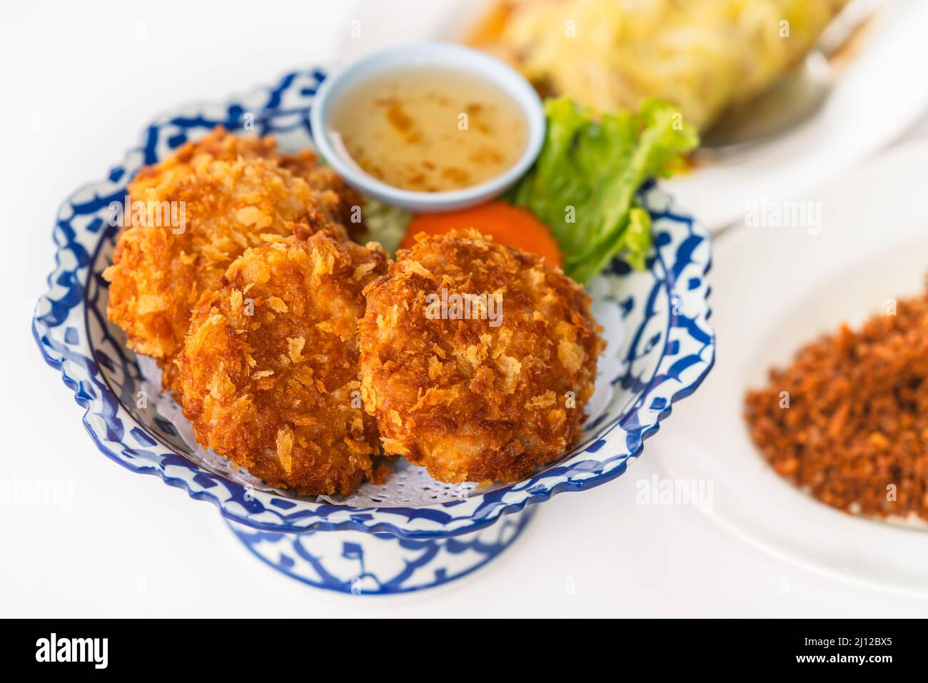 Deep-fried shrimp Cake on a beautiful plate with plum sauce, close-up image of deep-fried shrimp cake with blurred other food on white background, an Stock Photo