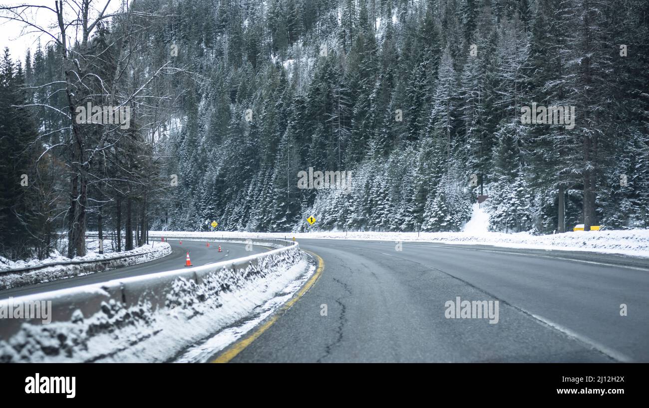 Scenic winter dangerous icy slippery winding highway road with piles of snow on the side of the road after clearing the road and snow-covered mountain Stock Photo