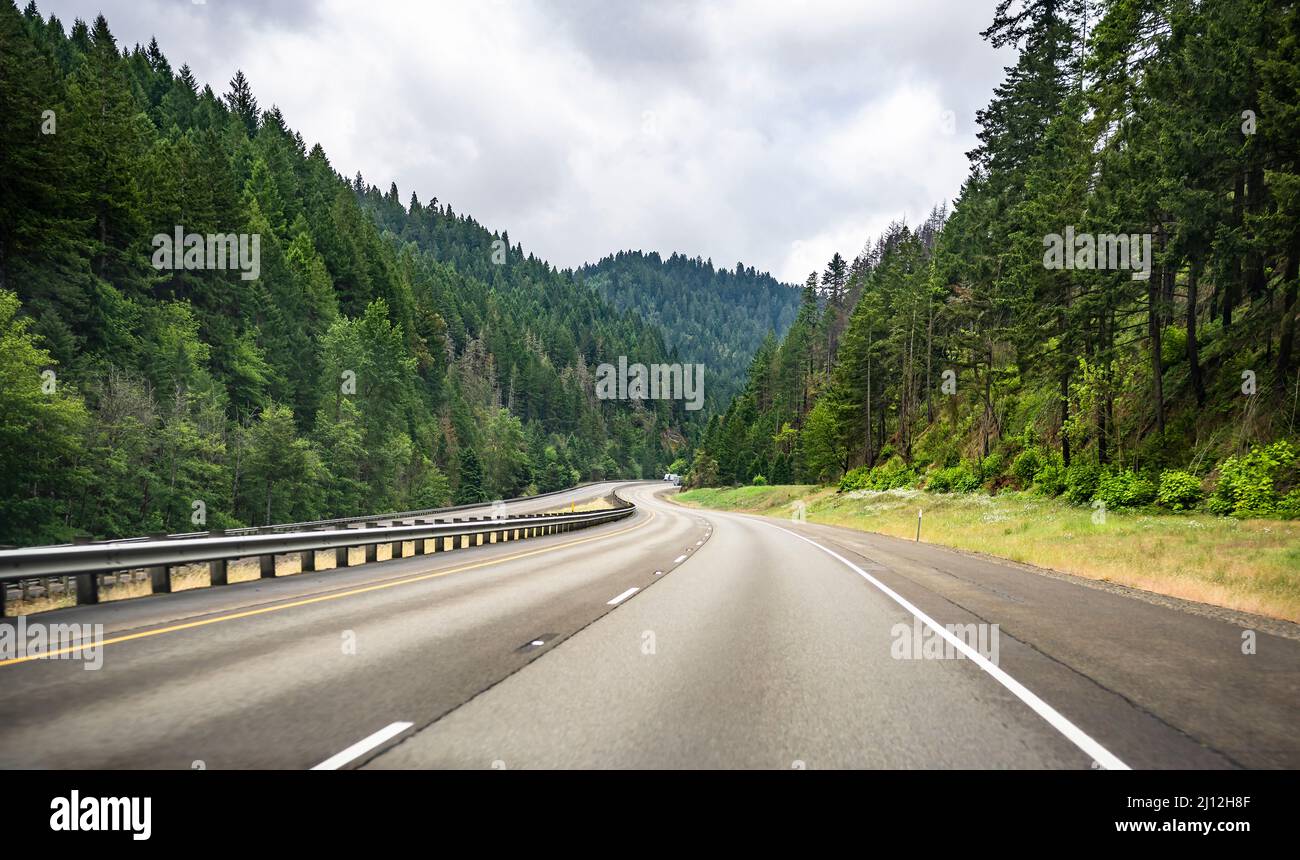 Scenic summer landscape with a disappearing around the corner winding mountain highway road with markings and a security divided fence and green fores Stock Photo