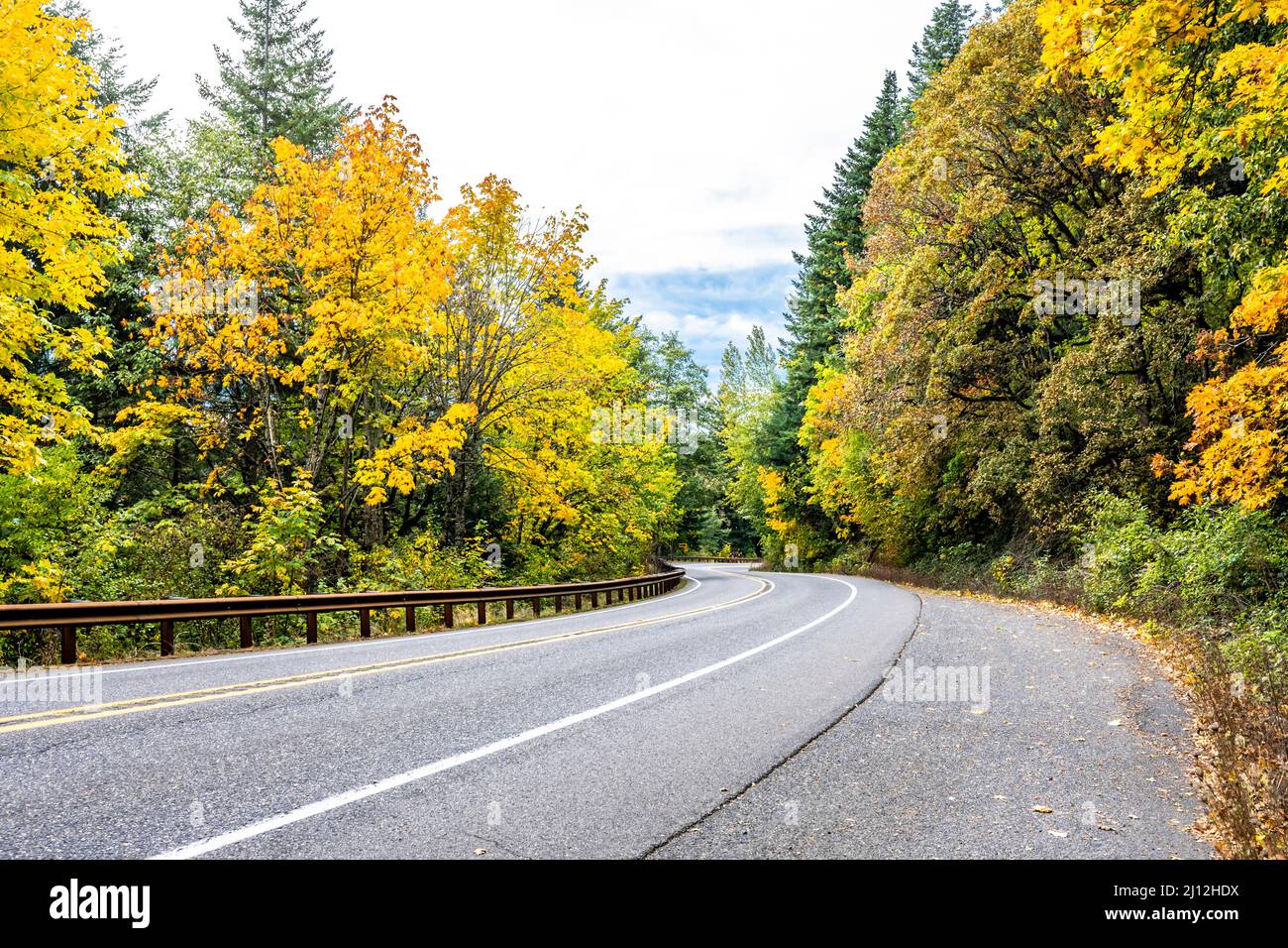Scenic autumn landscape with a disappearing around the corner winding mountain road with markings and a security fence and yellowed forest trees on th Stock Photo