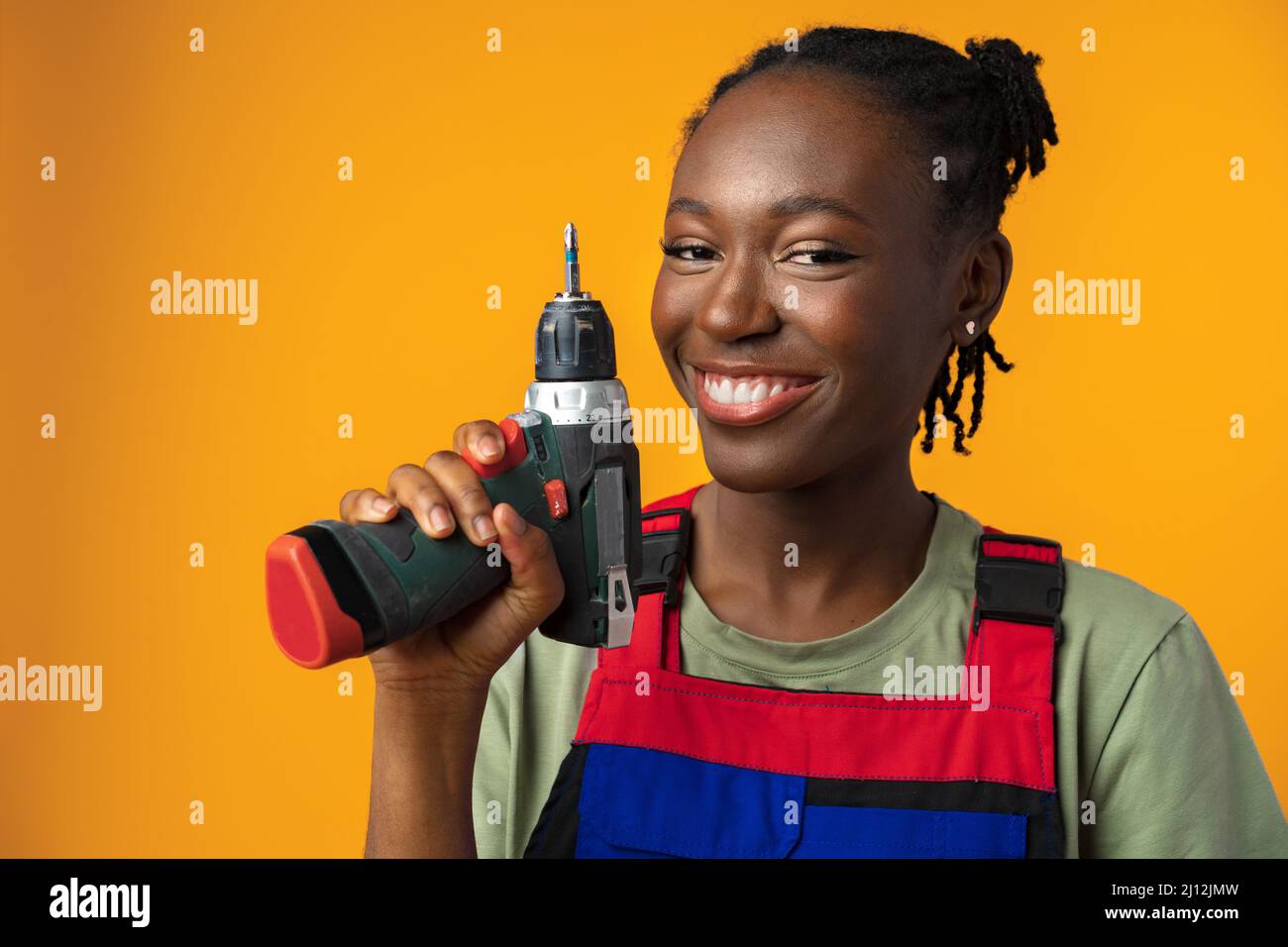 Black African American female model in uniform holding a screwdriver repair tool against yellow background Stock Photo
