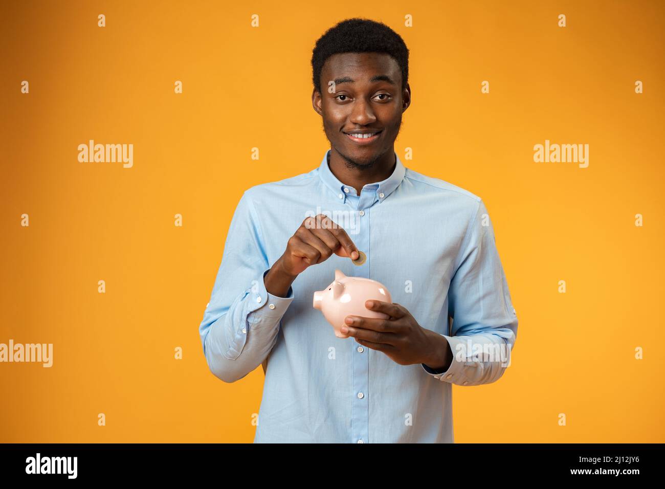 Young african amercian man holding piggy bank over yellow background Stock Photo
