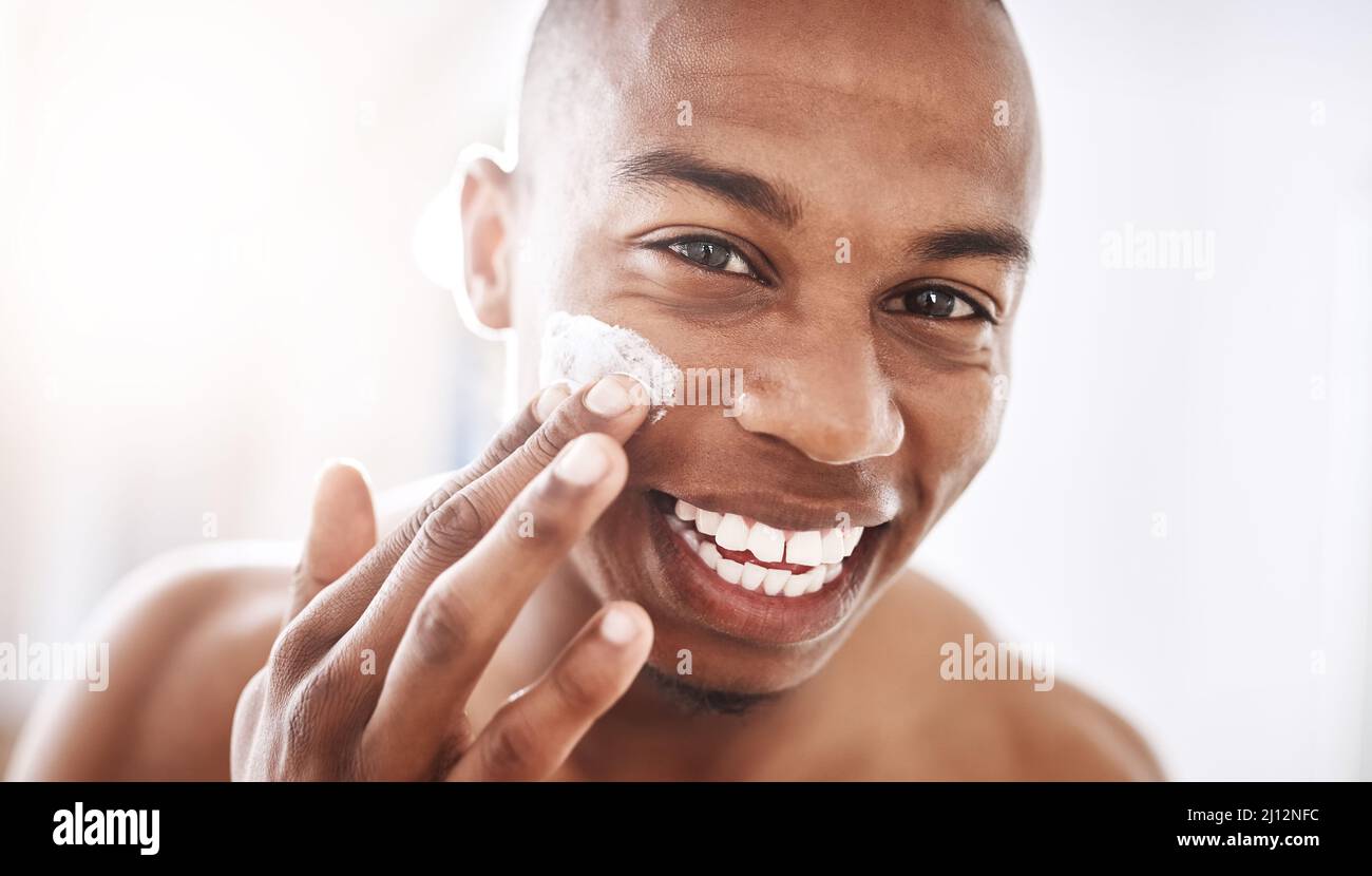 Ladies love a smooth talker with an even smoother face. Portrait of a handsome young man applying moisturizer to his face in the bathroom at home. Stock Photo