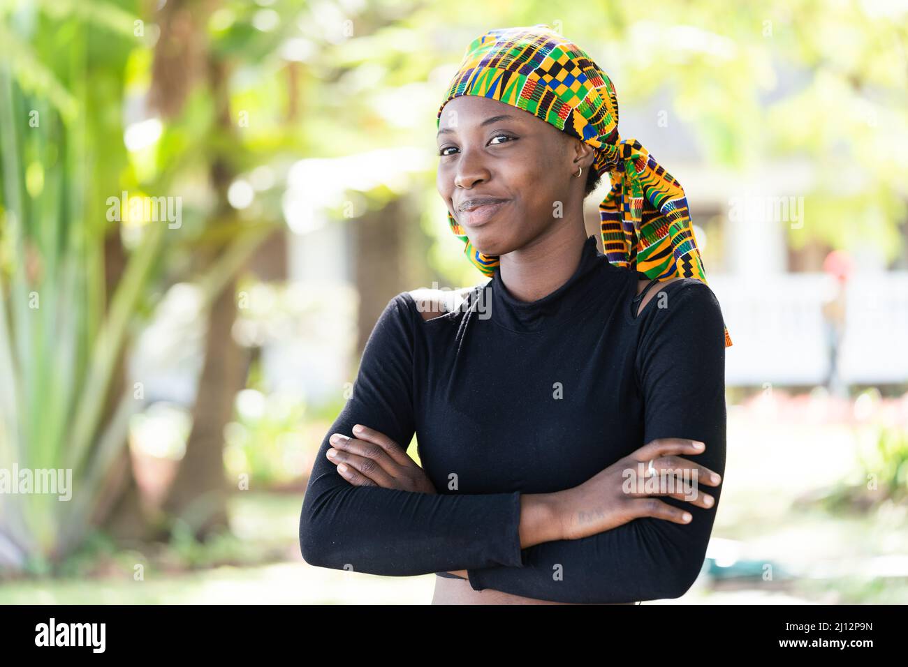 Smart young African beauty wearing a colorful, knotted scarf on her head and a black turtleneck sweater, smiling mischievously at the camera; symboliz Stock Photo